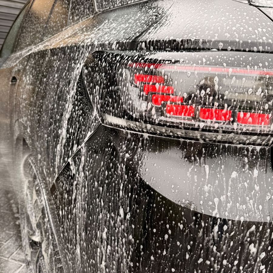 Snow foam clinging to the rear light cluster of a black car